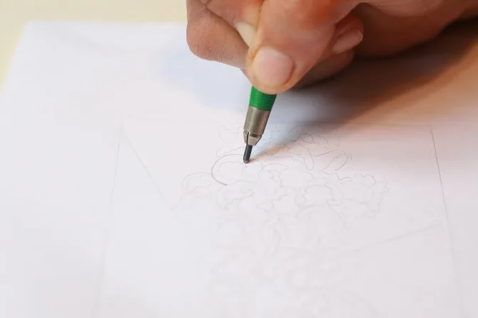 A hand drawing a cluster of flowers in pencil on a sheet of white paper.